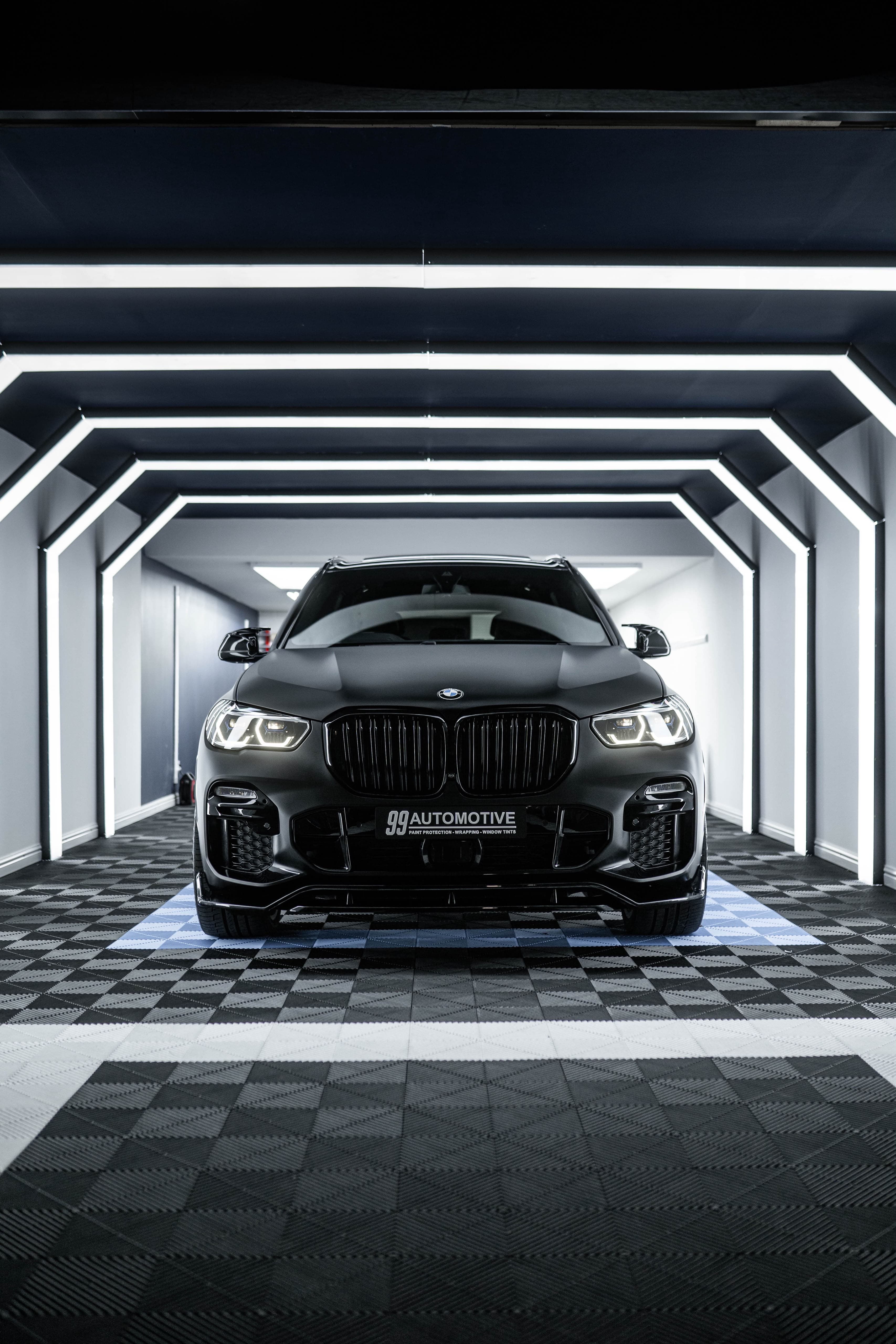 Matte black BMW X5, headlights on, nested LED arches
