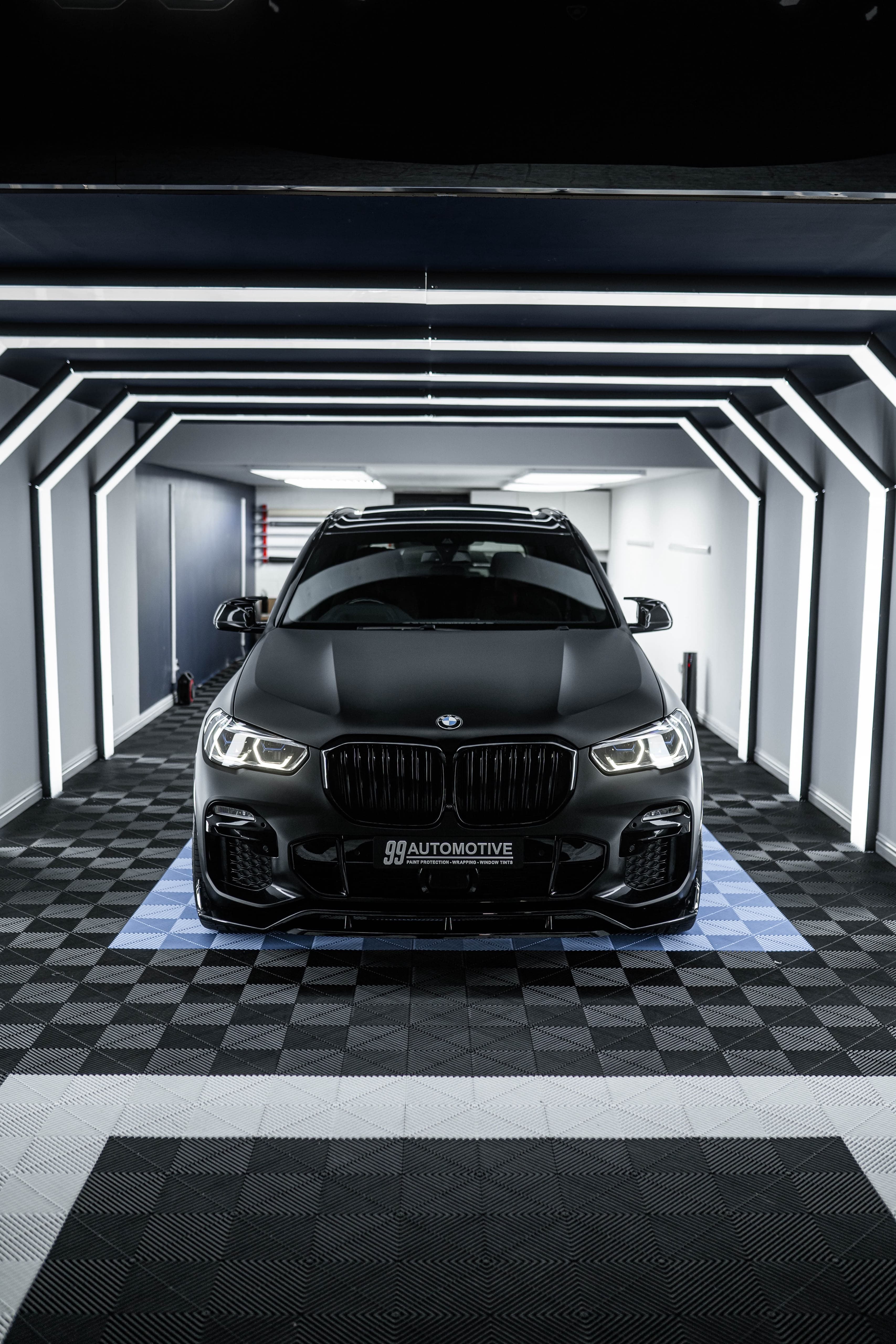 Matte black BMW SUV, front-on in the LED light tunnel