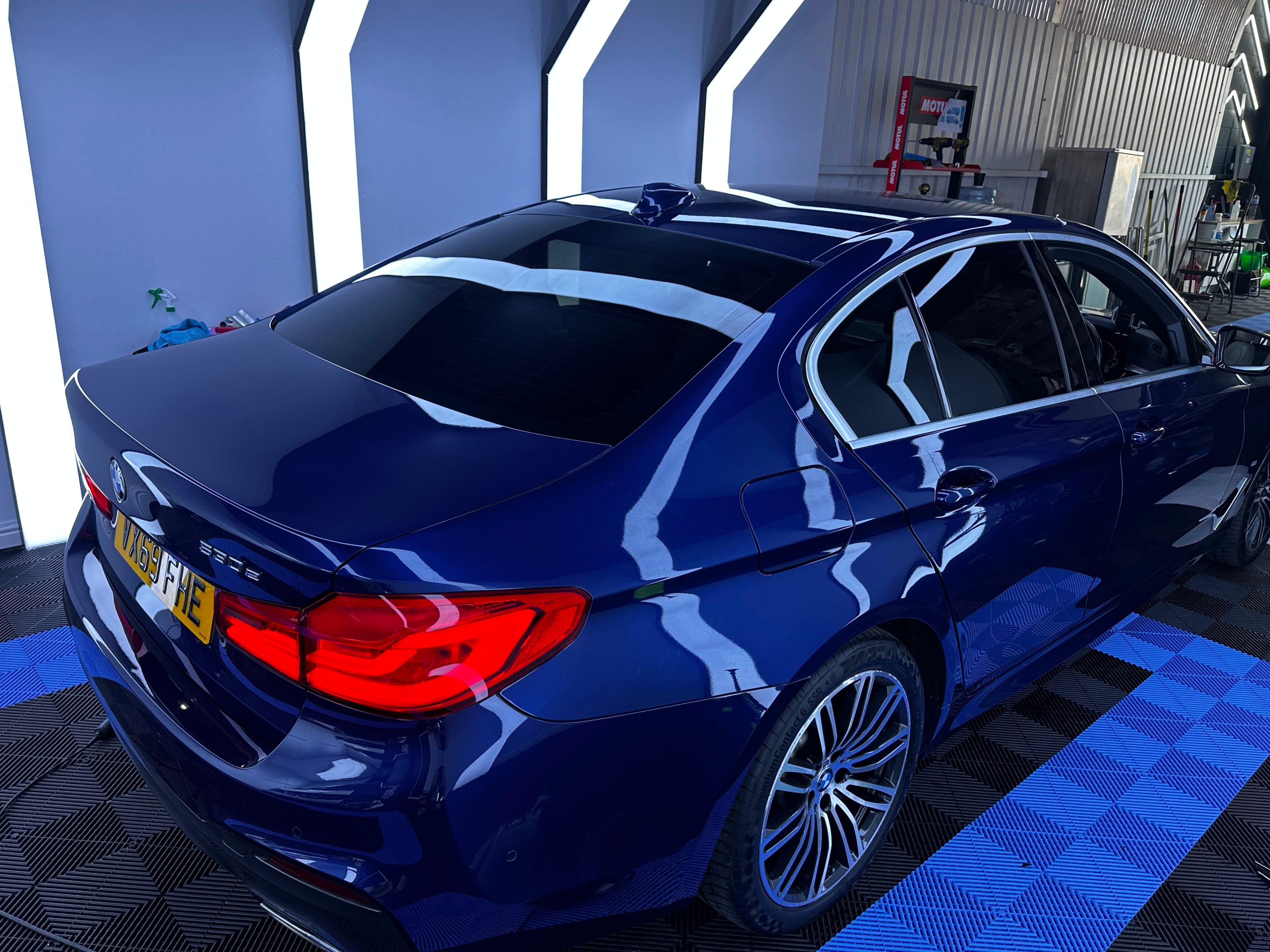 Metallic blue BMW 530e, rear three-quarter under studio LEDs